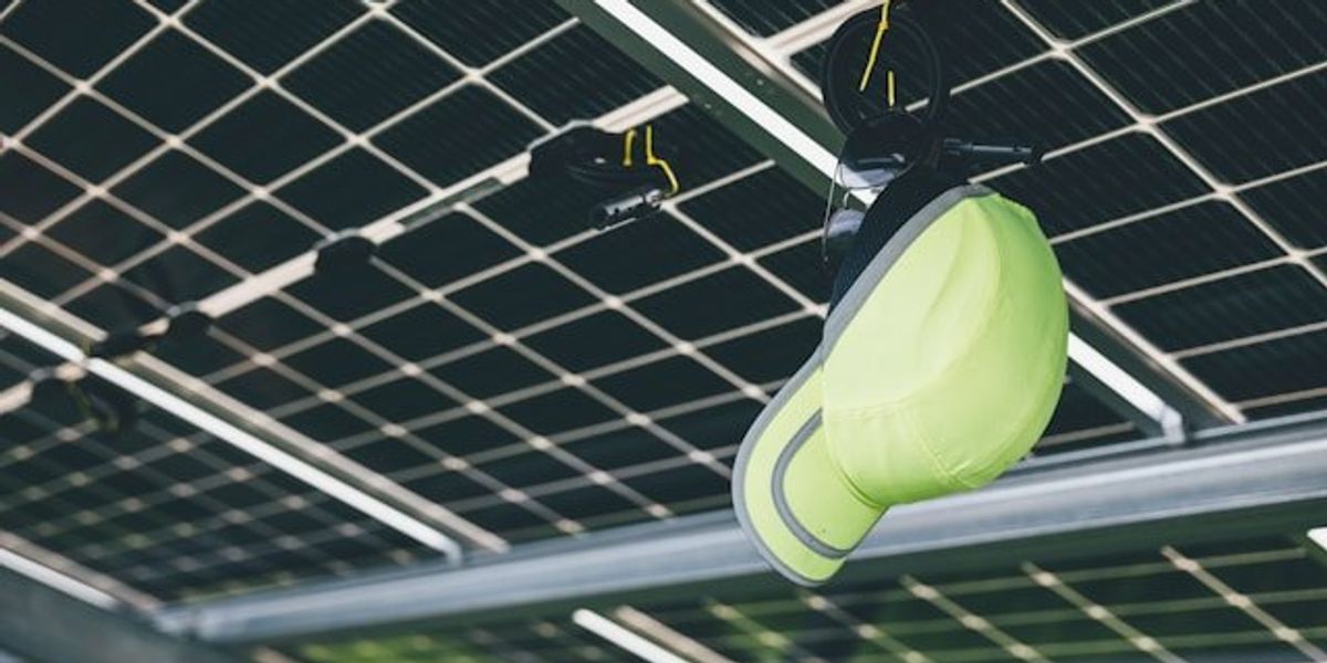 A lime green hat hanging on the underside of solar panels