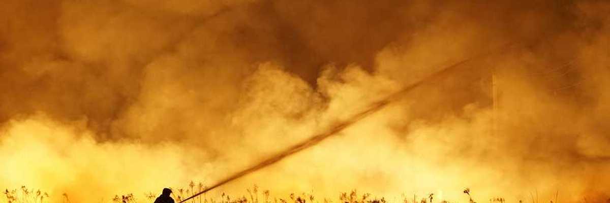 A lone firefighter training a stream of water on a huge wildfire