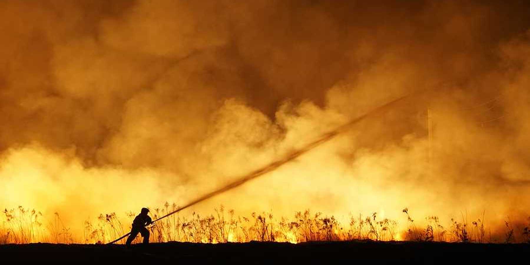 A lone firefighter training a stream of water on a huge wildfire