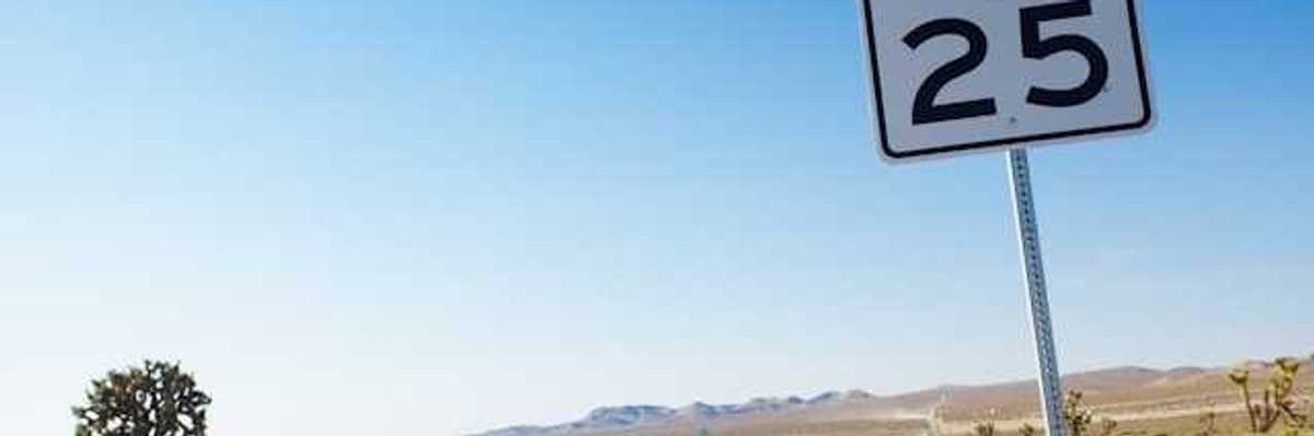 A long road stretching into a desert landscape with a speed limit sign showing 25 mph