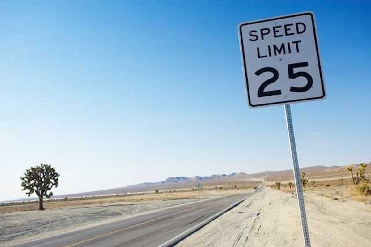 A long road stretching into a desert landscape with a speed limit sign showing 25 mph