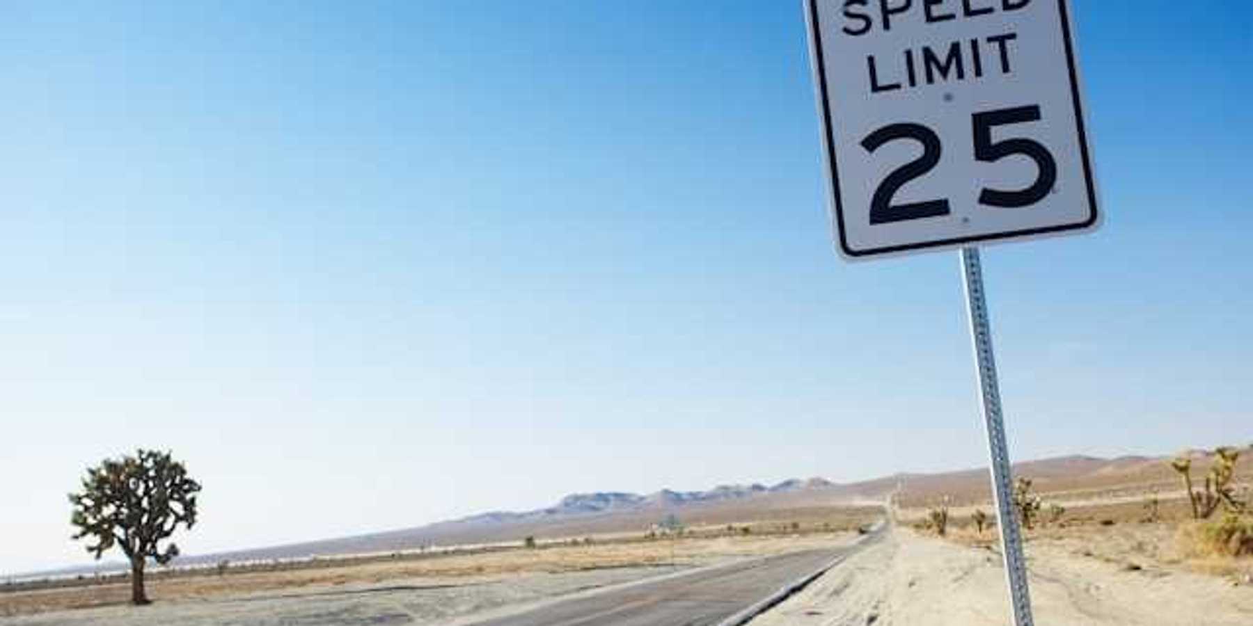 A long road stretching into a desert landscape with a speed limit sign showing 25 mph