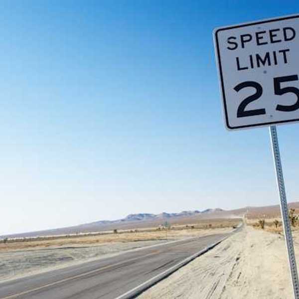 A long road stretching into a desert landscape with a speed limit sign showing 25 mph