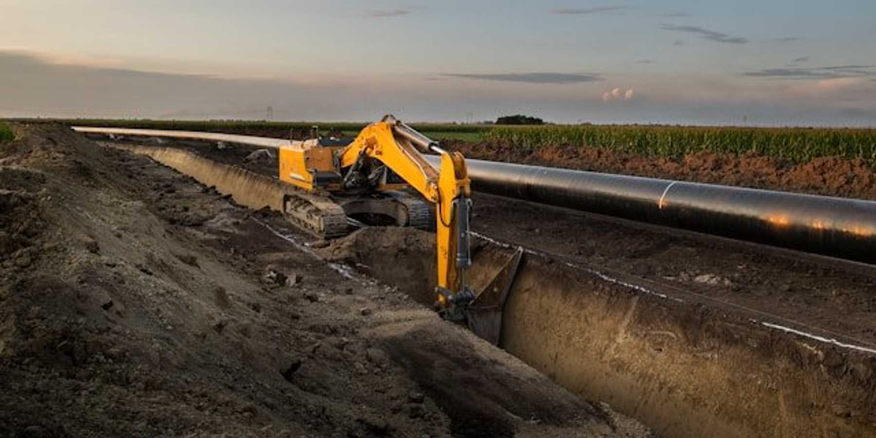A machine digging a trench for a pipeline alongside an agricultural field.