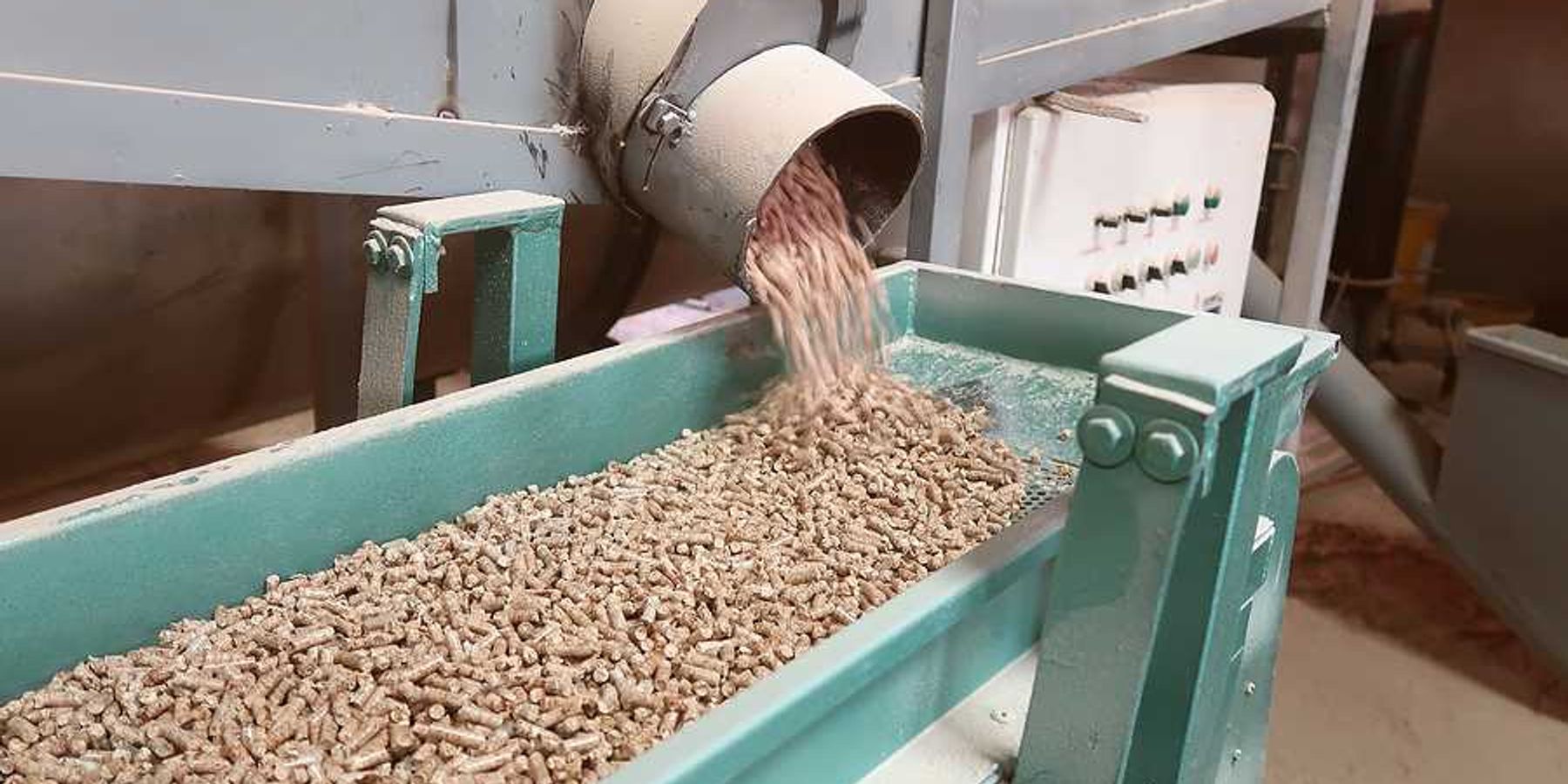 A machine dropping wood pellets into a green metal trough