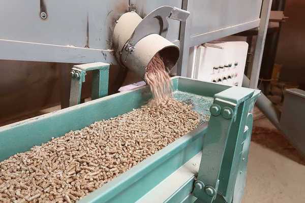 A machine dropping wood pellets into a green metal trough