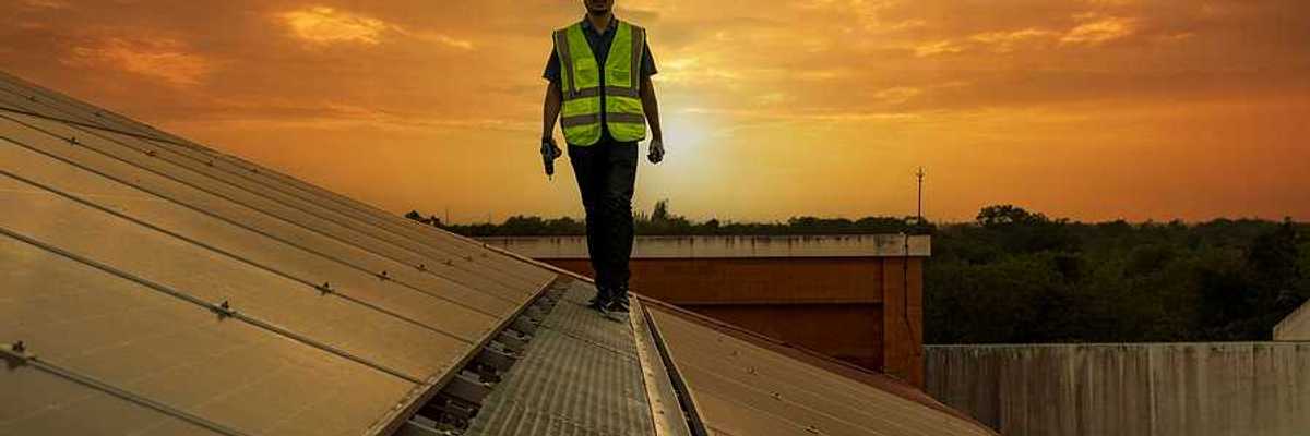 A maintenance worker walking along a solar panel with the sun in the background