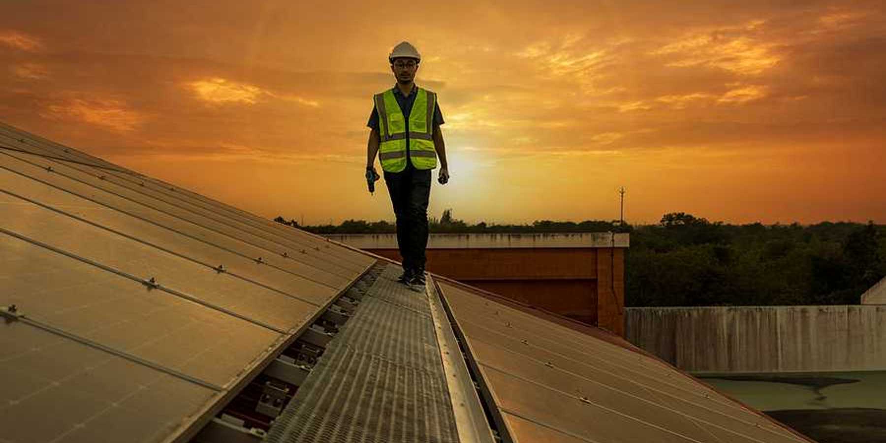 A maintenance worker walking along a solar panel with the sun in the background
