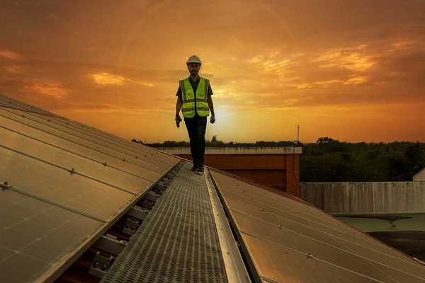A maintenance worker walking along a solar panel with the sun in the background