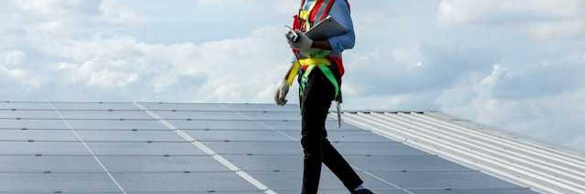 A maintenance worker walking alongside solar panels on a roof