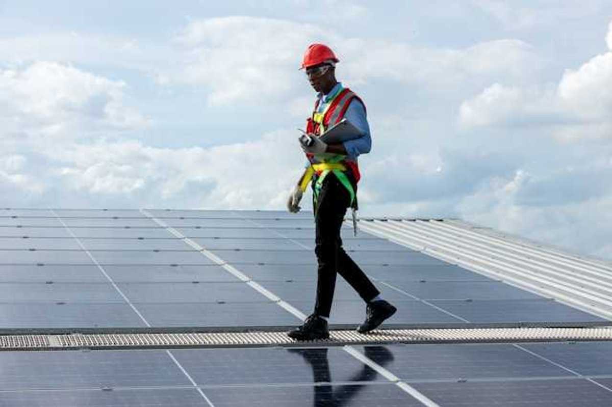 A maintenance worker walking alongside solar panels on a roof