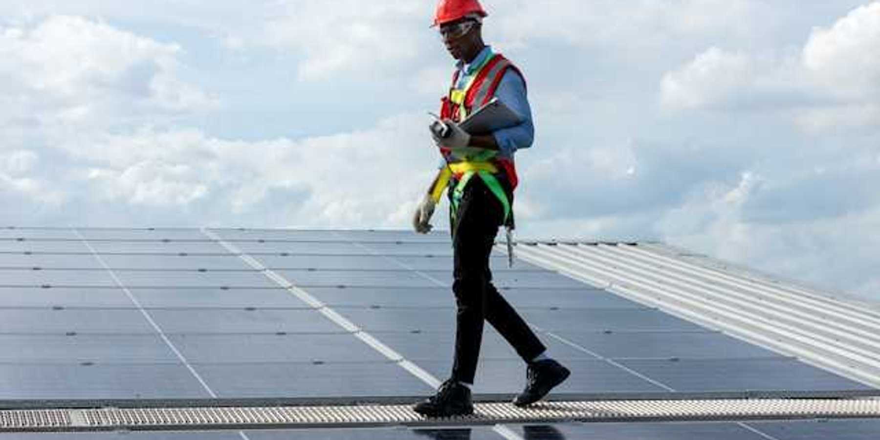 A maintenance worker walking alongside solar panels on a roof