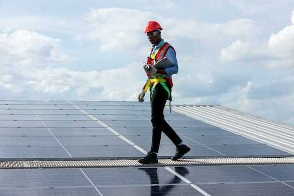 A maintenance worker walking alongside solar panels on a roof