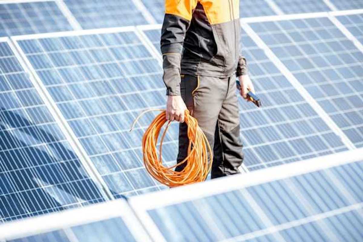 A maintenance worker wearing black standing in front of solar panels