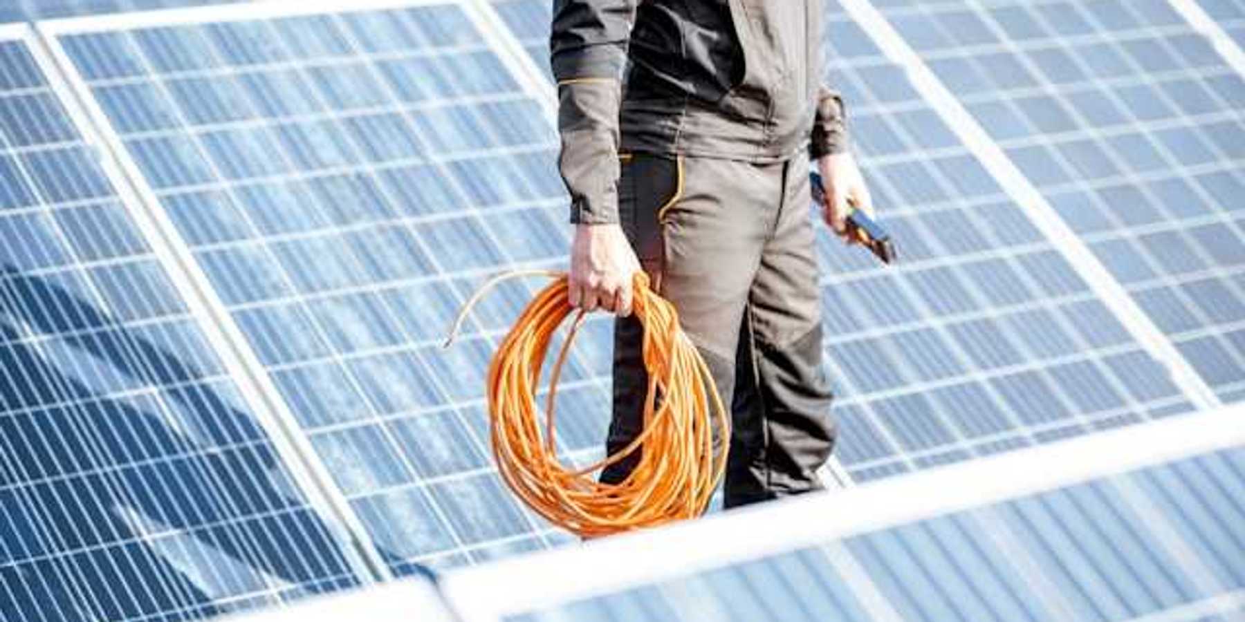 A maintenance worker wearing black standing in front of solar panels