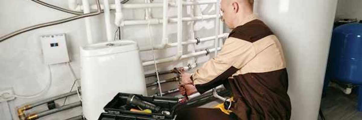 A man in a brown uniform with a tool box working on a heating system