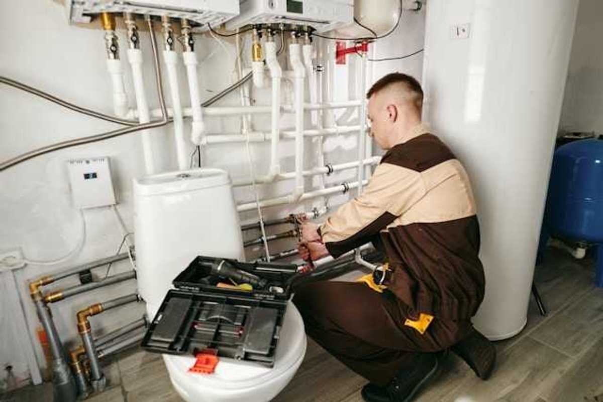 A man in a brown uniform with a tool box working on a heating system