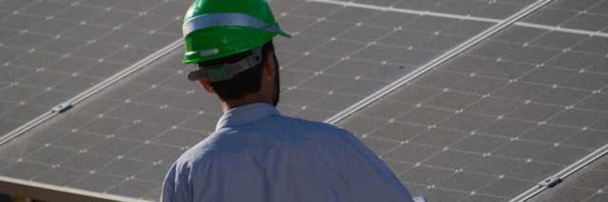 A man in a green hardhat looking at a solar panel