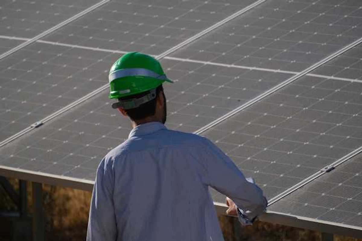 A man in a green hardhat looking at a solar panel