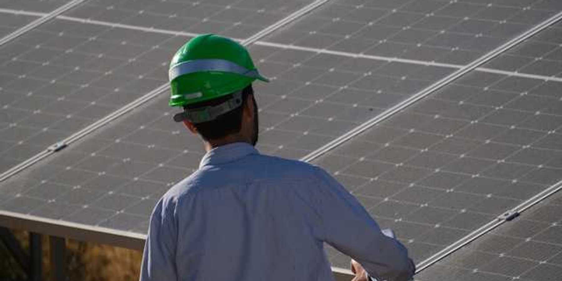 A man in a green hardhat looking at a solar panel