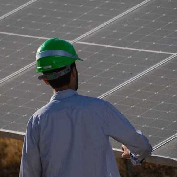 A man in a green hardhat looking at a solar panel