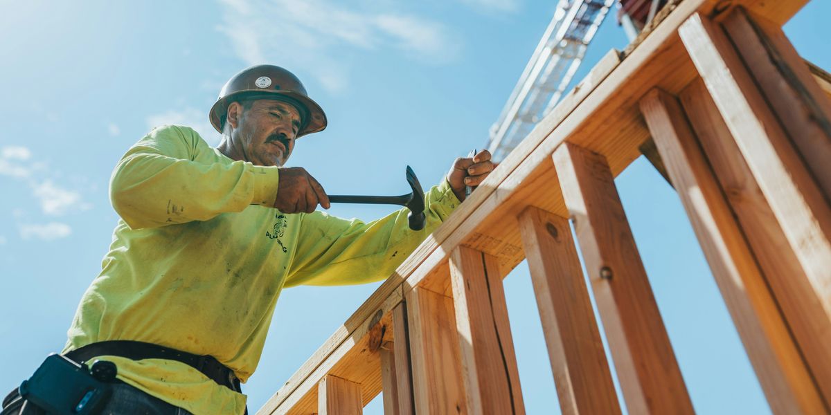 a man in a hard hat and safety gear working on a wooden structure.