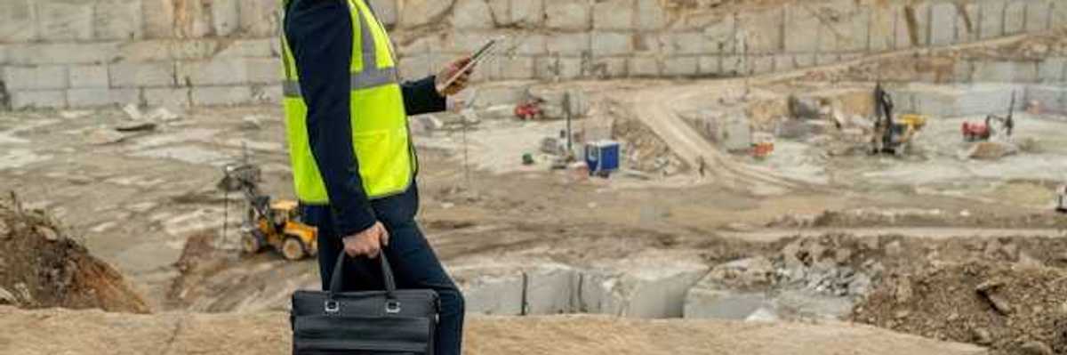 A man in a suit wearing a hard hat and a yellow vest at the edge of a pit
