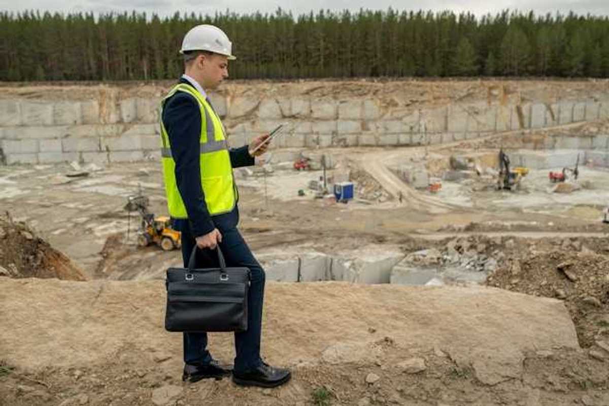 A man in a suit wearing a hard hat and a yellow vest at the edge of a pit
