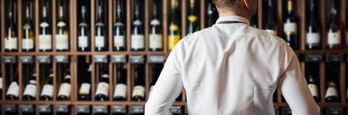 A man in a white shirt looking at a wall of wine bottles