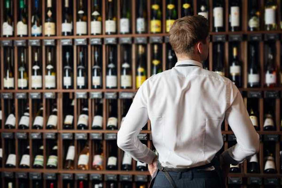 A man in a white shirt looking at a wall of wine bottles
