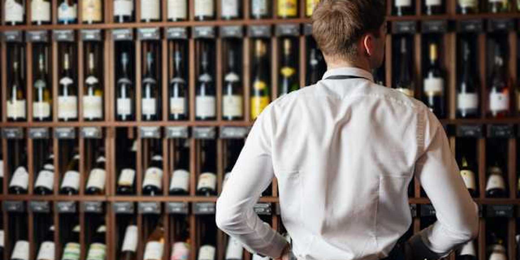 A man in a white shirt looking at a wall of wine bottles