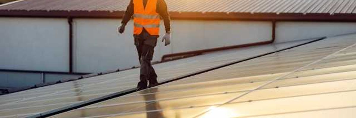 A man in an orange safety vest walking on a roof inspecting solar panels