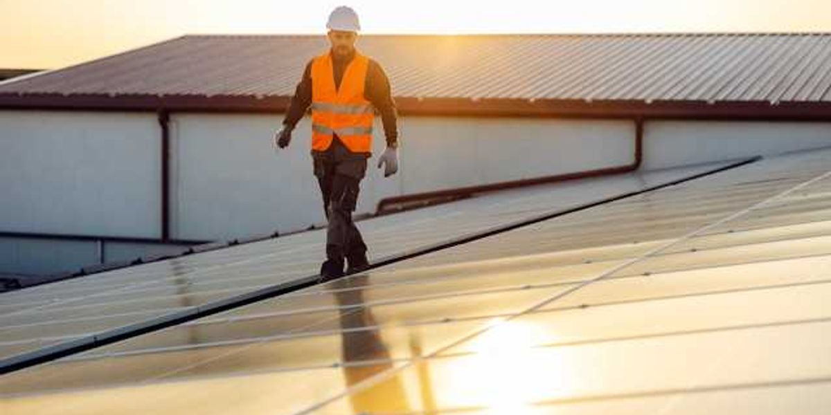 A man in an orange safety vest walking on a roof inspecting solar panels