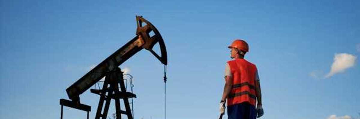 A man in an orange vest looking up at an oil pump jack