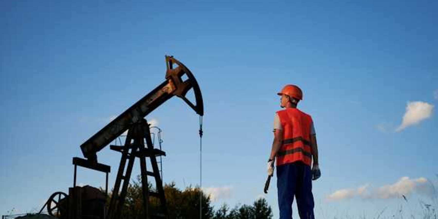 A man in an orange vest looking up at an oil pump jack