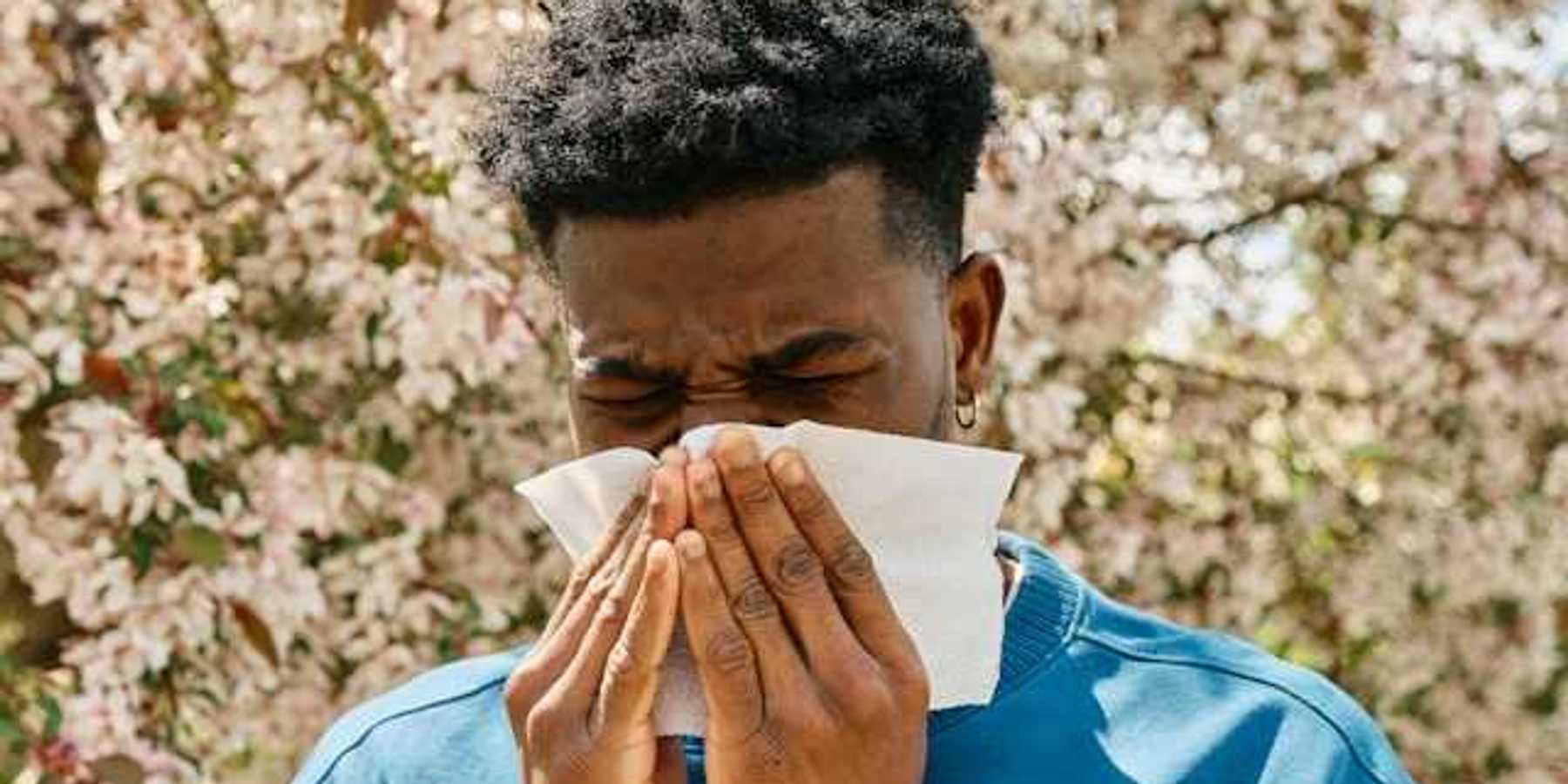 A man in front of a flowering tree blowing his nose