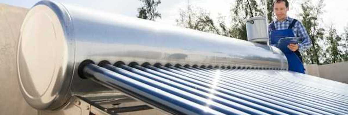 A man inspects a solar water heater on a roof