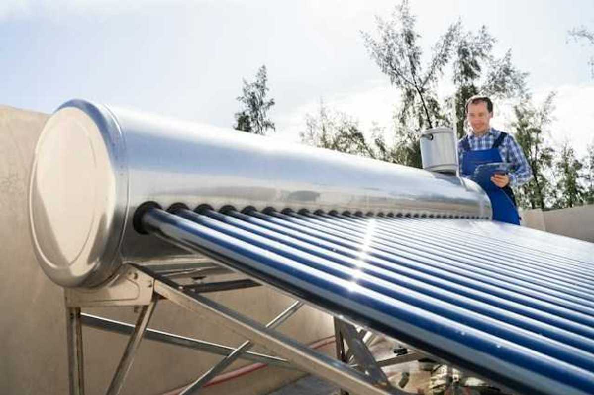 A man inspects a solar water heater on a roof