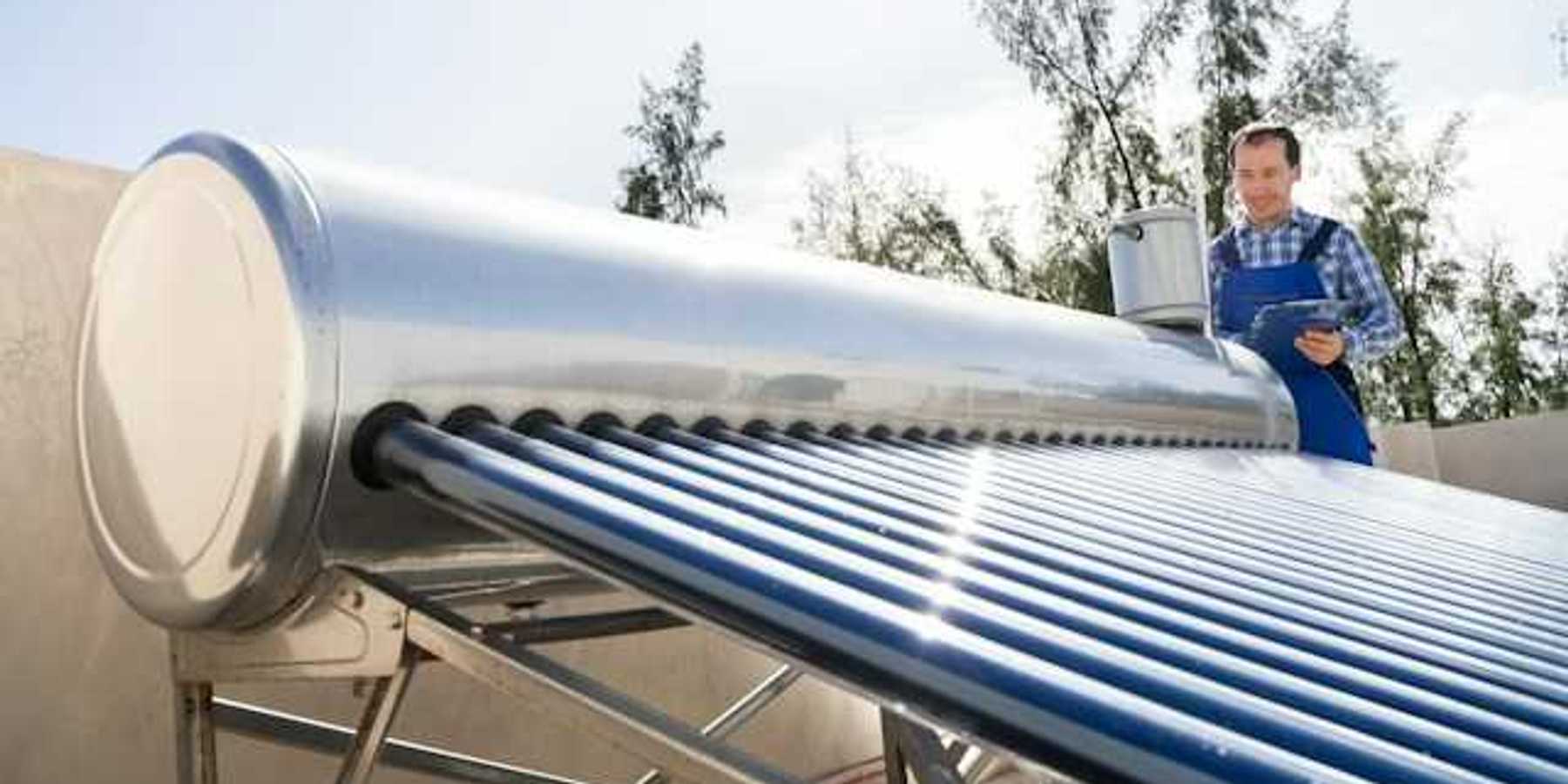 A man inspects a solar water heater on a roof