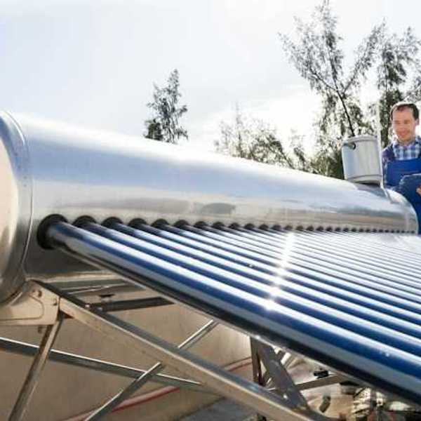 A man inspects a solar water heater on a roof