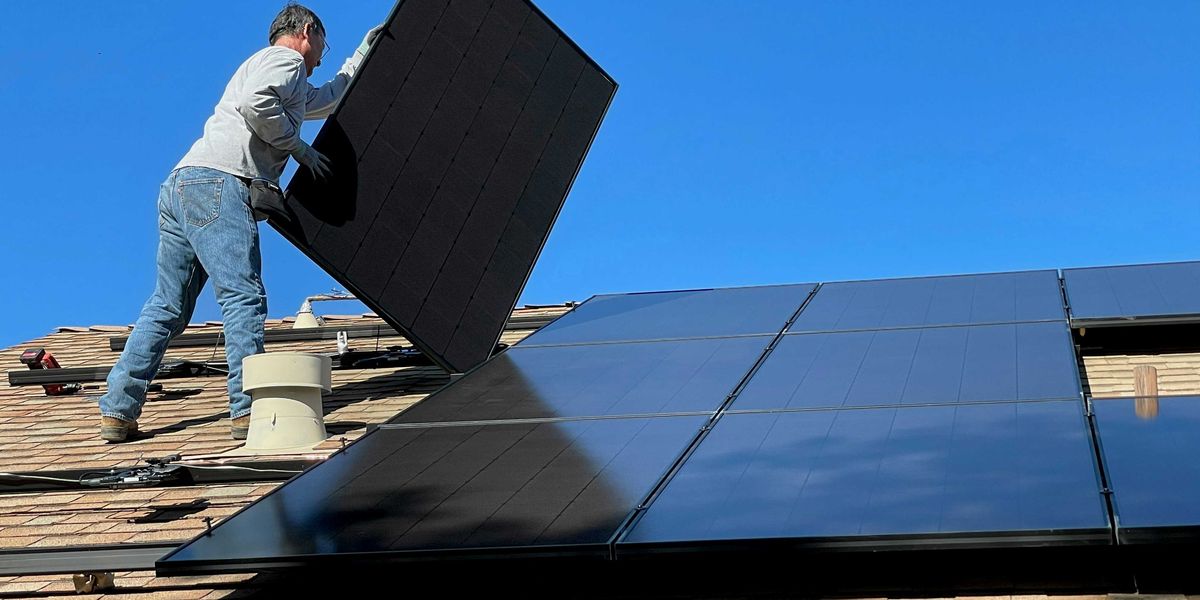 A man installs solar panels on a roof.