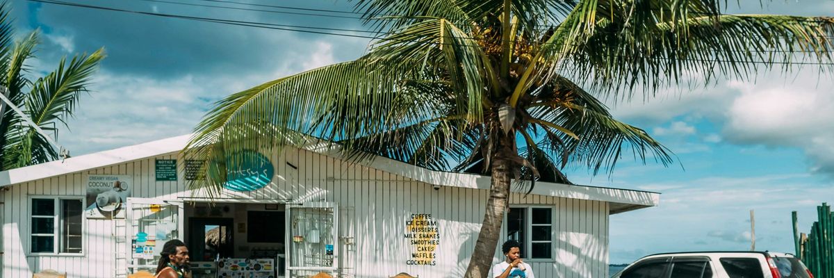 A man of African descent wearing a tank top riding bicycle in front of white building near palm tree during daytime.