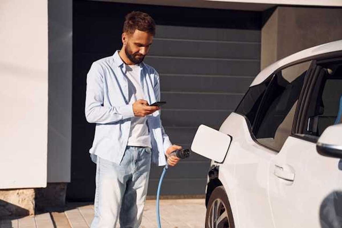 A man plugging in his electric vehicle outside his house