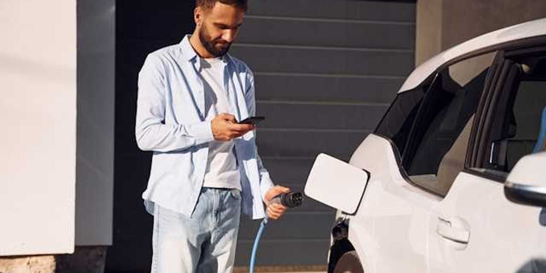 A man plugging in his electric vehicle outside his house