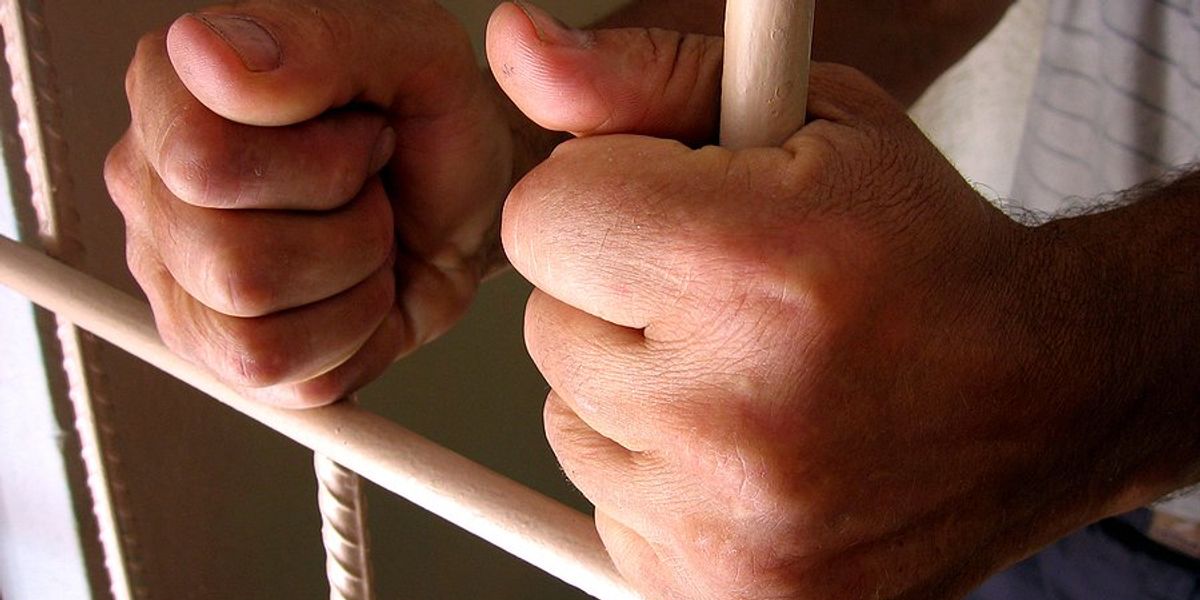 A man's hands holding the bars of a prison cell