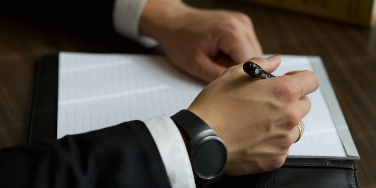 A man's hands with a pen writing on a pad of paper.