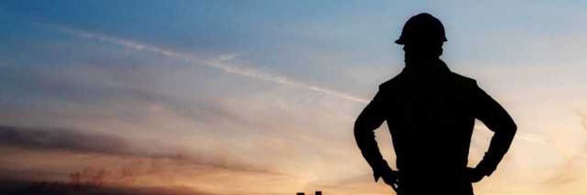 A man silhouetted against a darkening sky with smokestacks in the distance