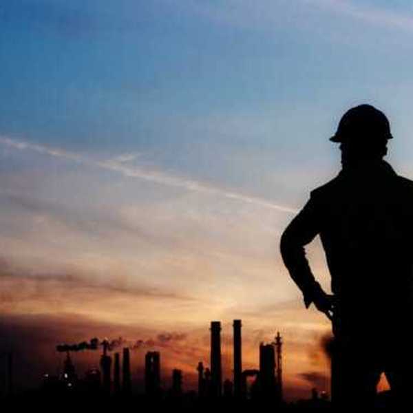 A man silhouetted against a darkening sky with smokestacks in the distance