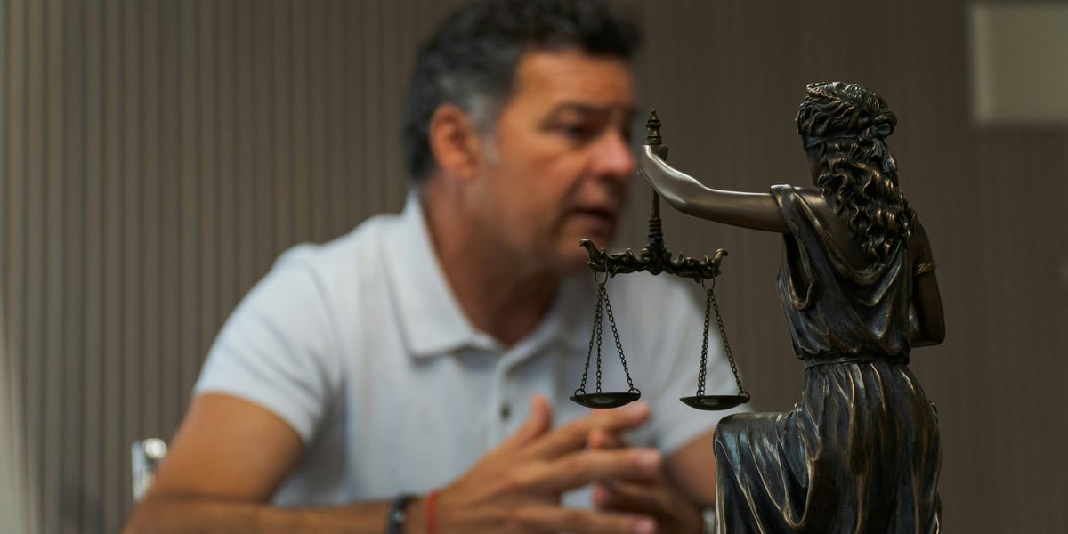 A man sitting at a table in front of a statue of Lady Justice.
