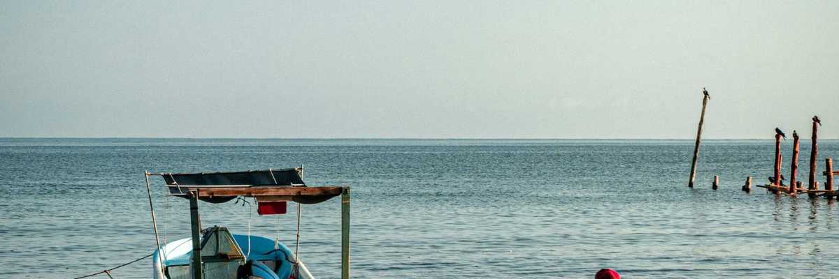 a man sitting on the shore of a beach next to a boat.